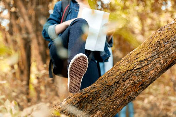 Close up shoe crossed over the tree.   Asian traveler with backpack adventure holding map to find directions and walking relax in the jungle forest outdoor for destination leisure nature on vacation. Travel  Concept - Foto, Imagem
