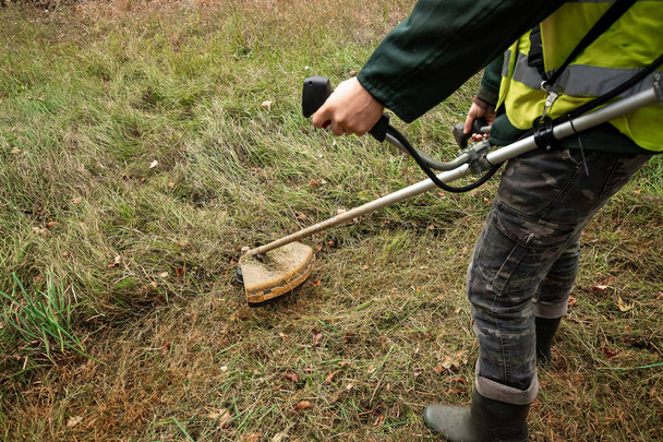 Un trabajador en traje profesional corta hierba con una podadora, una segadora. Cortando céspedes, bordes, bordes
 - Foto, Imagen