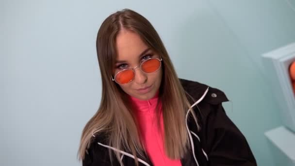 Fashionable girl in glasses on a turquoise background. Sits on a chair. Oranges on the bedside table - Footage, Video