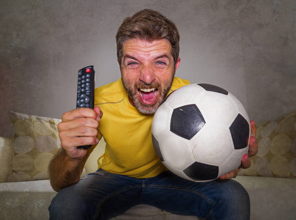 young happy and excited man watching European football game on TV celebrating goal on couch screaming spastic gesturing crazy cheerful as soccer fan enjoying victory - Fotó, kép