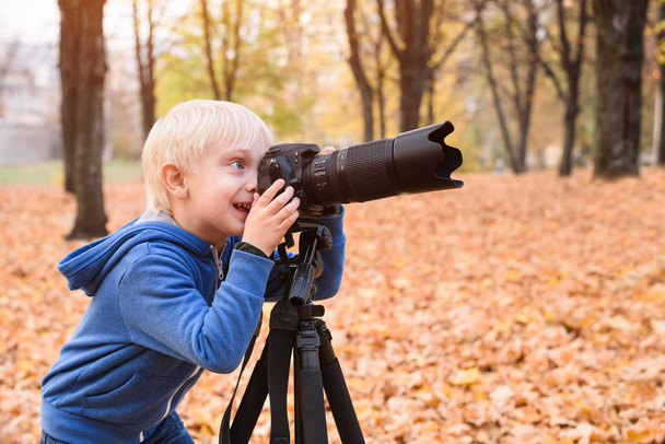 Mały blond chłopiec robi zdjęcia na lustrzankę. Jesienny Park - Zdjęcie, obraz