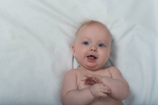 Portrait of a cute blond baby on a white sheet. Top view - 写真・画像