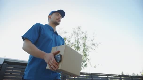 Beautiful Young Woman Meets Delivery Man who Gives Her Cardboard Box Package, She Signs Electronic Signature POD Device. Courier Delivering Parcel in the Suburban Neighborhood. Slow Motion Low Angle - Materiał filmowy, wideo
