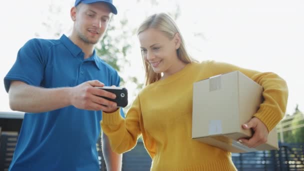 Young Woman Holding Delivered Cardboard Box Package, She Signs Electronic Signature POD Device and Says Goodbye to Delivery Man. Courier Delivering Parcel in the Suburban Neighborhood. Slow Motion - Metraje, vídeo