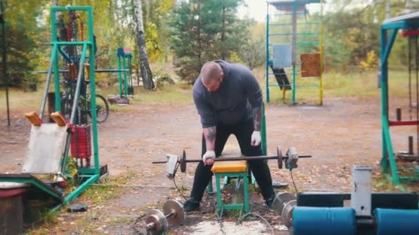 Un bodybuilder tatoué pompant ses mains avec les haltères faites de briques et de poids - entraînement sur le terrain de sport extérieur
 - Séquence, vidéo