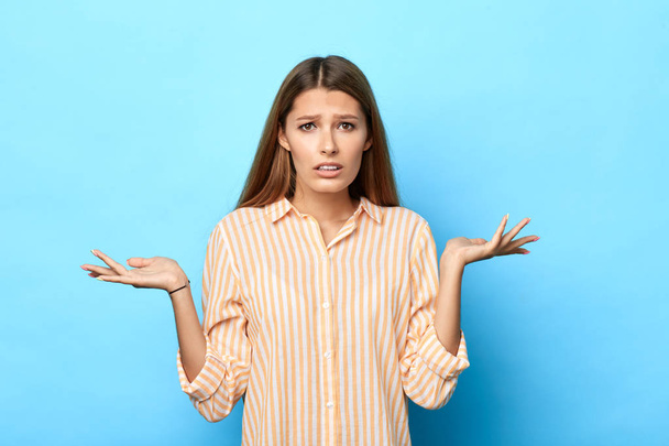 confused young brown-haired girl shrugging shoulders isolated over blue background - Foto, afbeelding