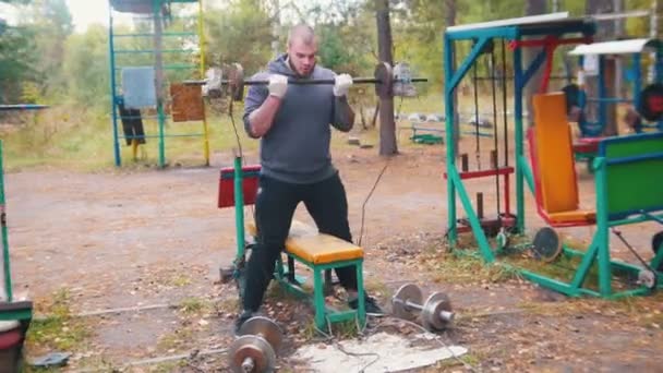 Un bodybuilder tatoué pompant ses mains avec les haltères faites de briques et de poids - entraînement sur le terrain de sport extérieur - forêt d'automne
 - Séquence, vidéo