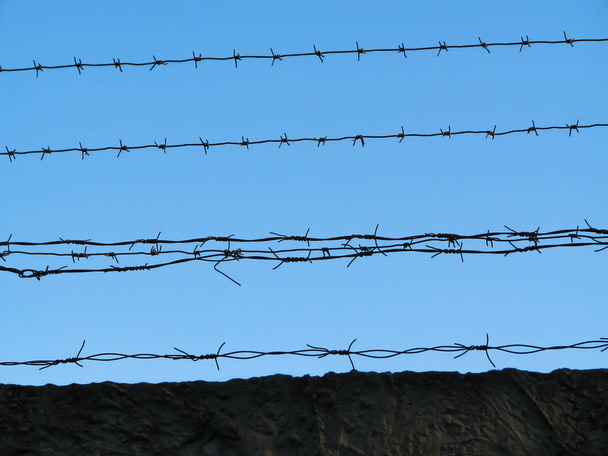 Несколько нитей старой ржавой колючей проволоки через бетонный забор
 - Фото, изображение