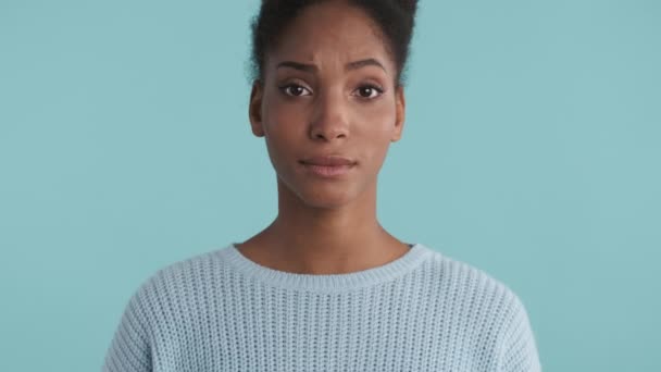Şaşırmış Afrikalı Amerikalı kızın portresi hayal kırıklığına uğramış bir şekilde mavi arka planda kameraya bakıyor. - Video, Çekim