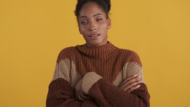 Portrait of offended casual afro-american girl in cozy sweater with crossed hands sadly looking around over yellow background - Footage, Video