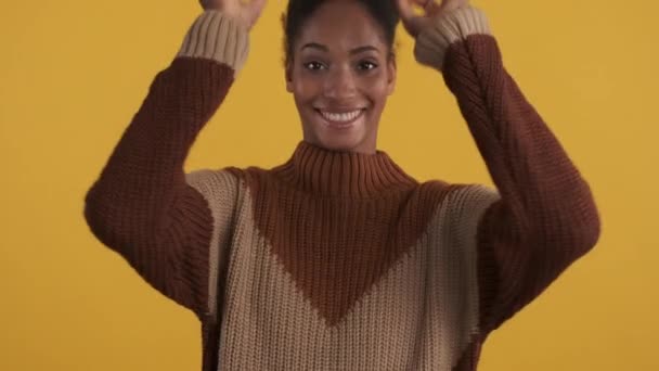 Πορτρέτο της χαρούμενης αφρικανικής κορίτσι σε πλεκτό πουλόβερ ευτυχώς κοροϊδεύουν γύρω από την κάμερα πάνω από κίτρινο φόντο - Πλάνα, βίντεο