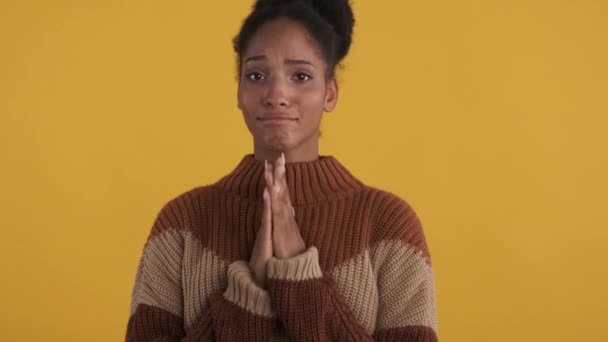 Çekici Afro-Amerikan kız rahat süveter giyer umarım jest yapar ve sarı arka plan üzerinde dua eder. - Video, Çekim