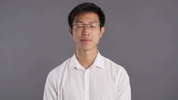 Jovem sorrindo asiático homem em óculos amigável acenando mão na câmera sobre fundo cinza
  - Filmagem, Vídeo