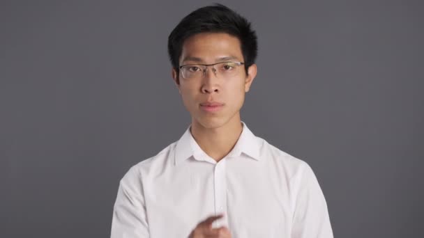Jovem sério asiático homem em óculos mostrando silêncio gesto na câmera sobre cinza fundo
  - Filmagem, Vídeo