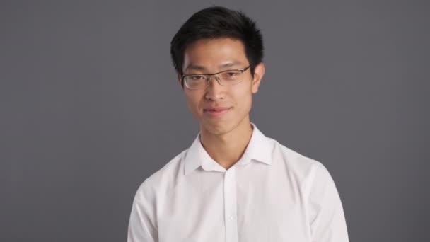 Jovem confiante asiático homem em óculos regozijando-se na câmera sobre fundo cinza. Expressão feliz
 - Filmagem, Vídeo