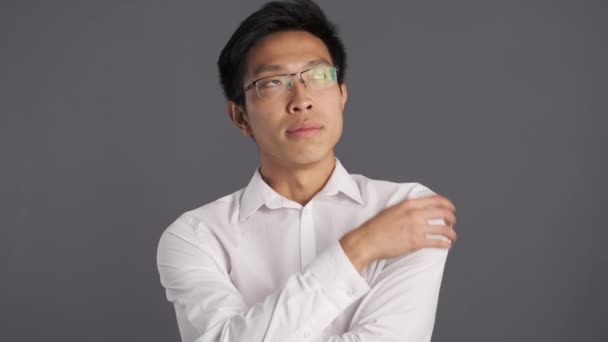 junger nachdenklicher asiatischer Mann mit Brille blickt nachdenklich in die Kamera vor grauem Hintergrund  - Filmmaterial, Video