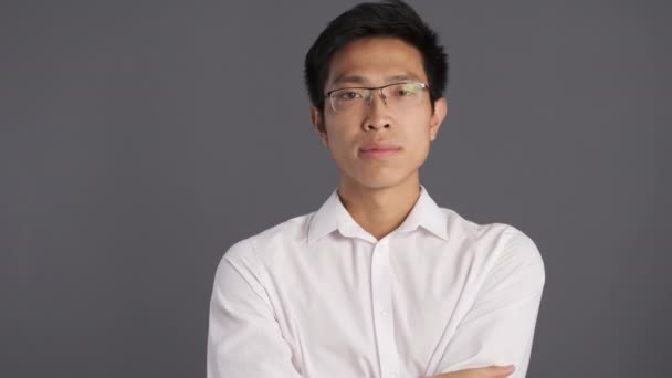 junger nachdenklicher asiatischer Mann mit Brille, der nachdenkt und mit dem Kopf wedelt, keine Geste vor der Kamera vor grauem Hintergrund  - Filmmaterial, Video