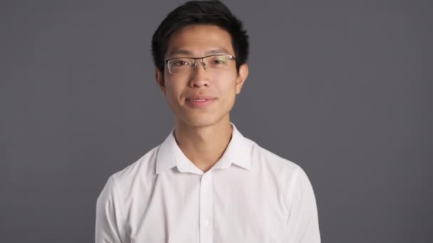 Joven sonriente asiático hombre en gafas felizmente mirando en cámara sobre gris fondo
  - Imágenes, Vídeo
