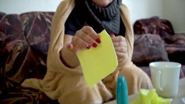 άρρωστη καυκάσια γυναίκα κάτω από μια κουβέρτα φυσάει τη μύτη της σε μια χαρτοπετσέτα στο σπίτι - Πλάνα, βίντεο