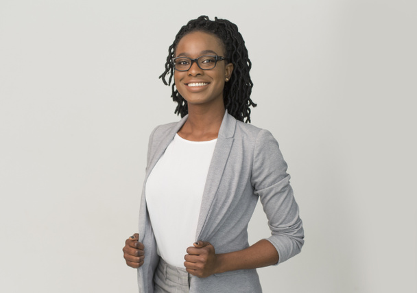 Negro mujer de negocios sonriendo en la cámara de pie sobre fondo gris
 - Foto, Imagen