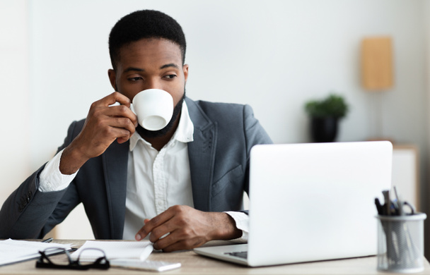 Mann trinkt Kaffee, während er im modernen Büro am Laptop arbeitet - Foto, Bild