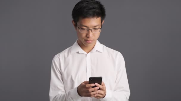 Серйозний азіатський чоловік в окулярах за допомогою мобільного телефону дратує сказати, що на камеру
 - Кадри, відео
