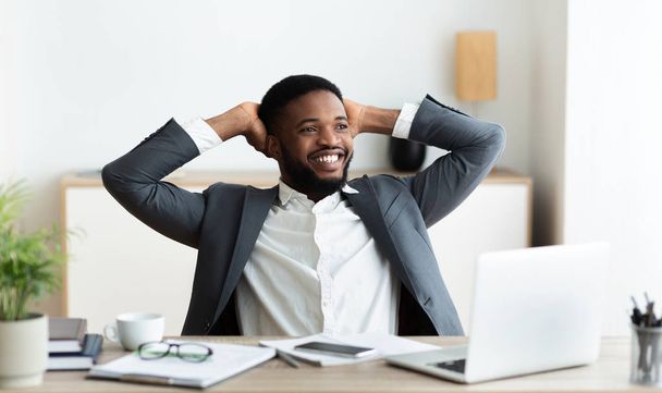 Homme d'affaires noir se détendre sur le lieu de travail, penché en arrière dans la chaise
 - Photo, image