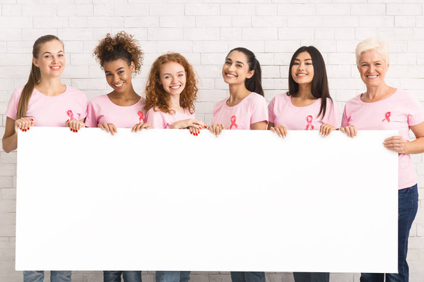 Donne in rosa T-shirt tenendo bordo bianco oltre muro di mattoni
 - Foto, immagini