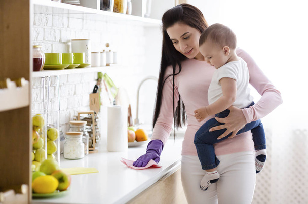 Młoda matka z Baby Boy sprzątanie kuchni w domu - Zdjęcie, obraz