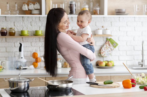 Το μωρό γελάει στα χέρια της μάνας, στην κουζίνα. - Φωτογραφία, εικόνα