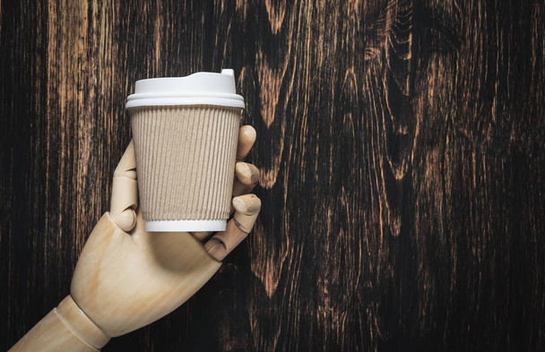 Une main en bois tient une tasse en papier pour le café ou le thé
. - Photo, image
