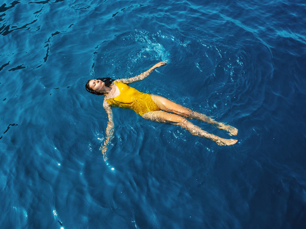 young woman in a one-piece yellow swimsuit floats on the surface of the water. - Фото, изображение