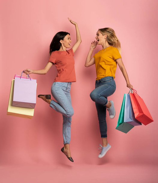 Two girls are happy after shopping. Joyful expression. Shop concept. Pink background - Photo, Image
