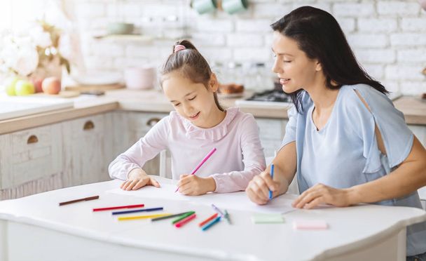 Mutter zeichnet mit Tochter auf Küchentisch - Foto, Bild