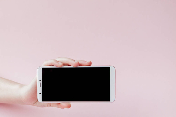 Modern mobile phone in a woman's hand on pink background - Foto, afbeelding