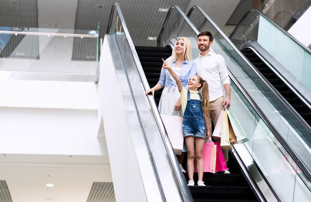 Dziewczyna pokazuje coś do rodziców stoi na schodach w hipermarkecie - Zdjęcie, obraz