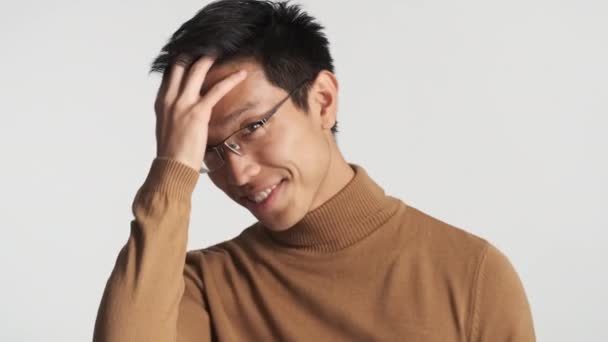 Jeune homme asiatique élégant attrayant dans les lunettes redresse heureusement les cheveux sur la caméra isolée. Maître de ramassage
 - Séquence, vidéo