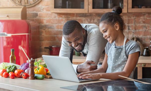 Усміхнений тато і дочка шукають рецепт, використовуючи ноутбук
 - Фото, зображення