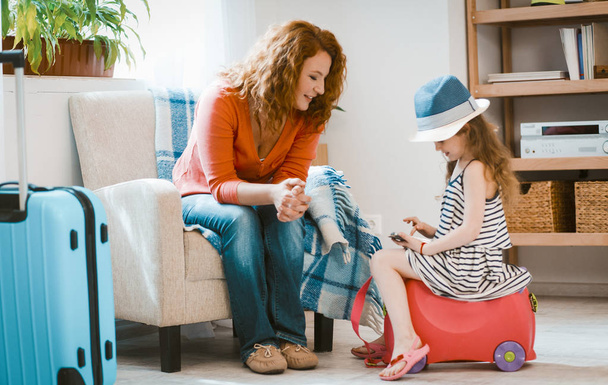 Family travel, mom and daughter sitting at home ready to leave. - 写真・画像