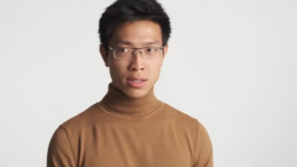 Молодой стильный азиатский мужчина в очках на белом фоне. Что происходит?
 - Кадры, видео
