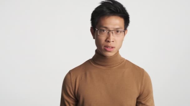 Mladý zuřivý asijský muž v brýlích zuřící na kameře nad bílým pozadím. Divoký naštvaný výraz - Záběry, video