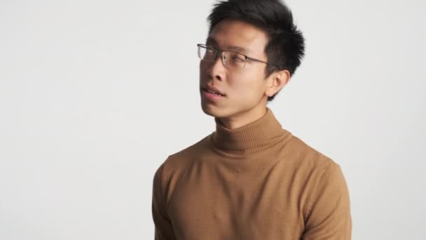 Jeune homme asiatique ennuyé dans les lunettes de vue en colère regardant autour sur fond blanc
 - Séquence, vidéo