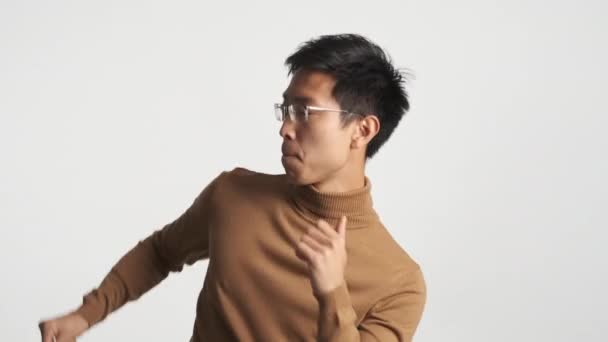 Young attractive stylish asian man in eyeglasses emotionally dancing enjoying moves isolated - Footage, Video