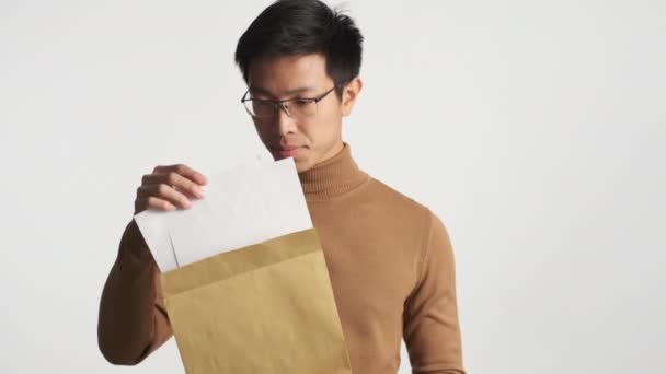 Young asian student opening envelope with exams results and getting angry on camera isolated - Materiał filmowy, wideo
