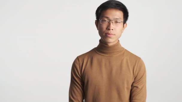 Fiatal jóképű, elegáns ázsiai férfi szemüvegben figyel és boldogan egyetért a kamerával elszigetelt - Felvétel, videó