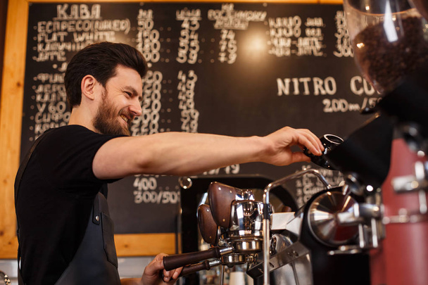 Young smiling male barista making coffee using professional coffee machine. Morning cup of coffee in caf. Coffee shop concept. - Foto, Imagen