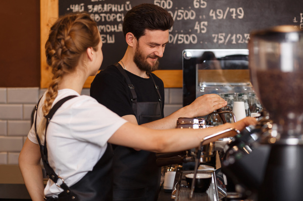 Two young smiling barista at work. Professional barista team brewing coffee using coffee machine in coffee shop. Happy young man and woman developing own coffee business. Coffee shop concept. - Photo, Image