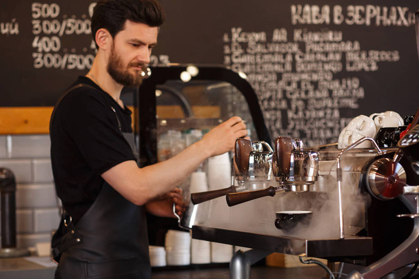Young smiling male barista making coffee using professional coffee machine. Morning cup of coffee in caf.  Coffee shop concept. - Foto, Imagen