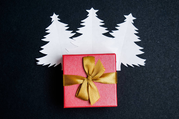 Caixa de presente com uma fita de ouro em árvores de Natal feita de papel branco sobre um fundo preto
. - Foto, Imagem