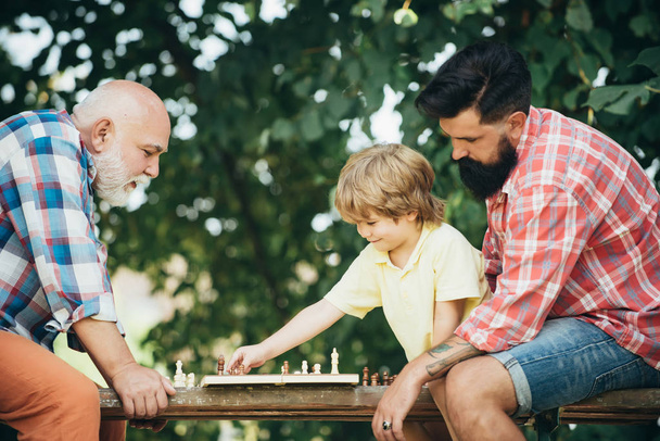 Η ιδέα της μέρας των πατέρων. Ο πρεσβύτερος διδάσκει στον εγγονό του να παίζει σκάκι. Ευτυχισμένος άνθρωπος οικογένεια ιδέα παίζοντας σκάκι και να διασκεδάσουν μαζί. - Φωτογραφία, εικόνα